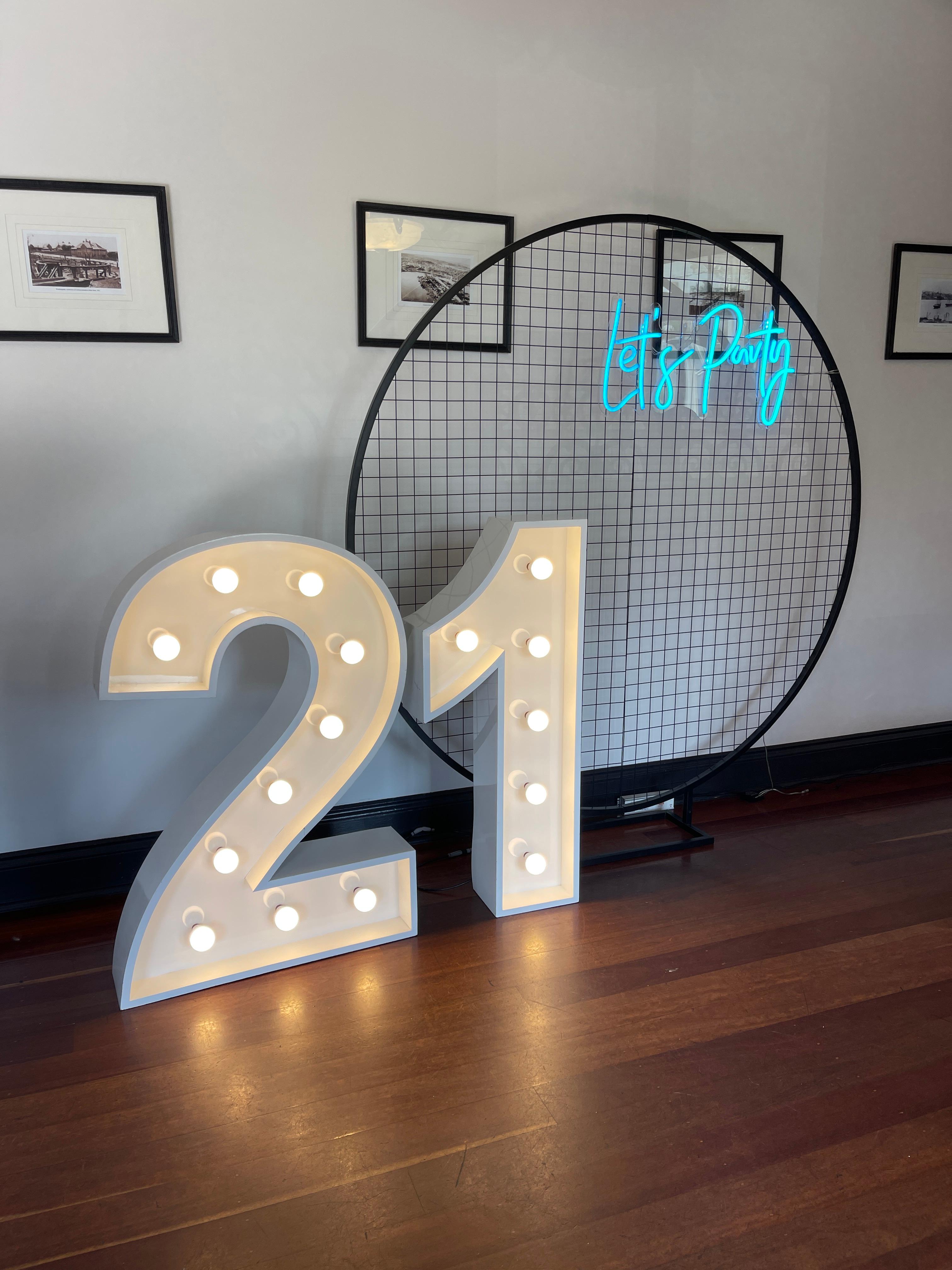 black circular mesh stand with 21 light up numbers and 'Let's party' neon sign